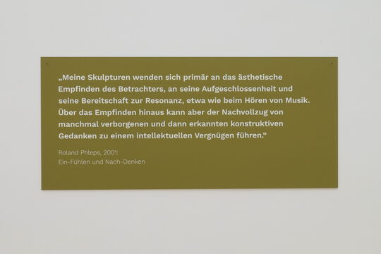 Text-Tafel: "Meine Skulpturen wenden sich primär an das ästhetische Empfinden des Betrachters, an seine Aufgeschlossenheit und seine Bereitschaft zur Resonanz, etwa beim Hören von Musik. Über das Empfinden hinaus kann aber der Nachvollzug von manchmal verborgenen und dann erkannten konstruktiven Gedanken zu einem intellektuellen Vergnügen führen." Roland Phleps, 2001: Ein-Fühlen und Nach-Denken