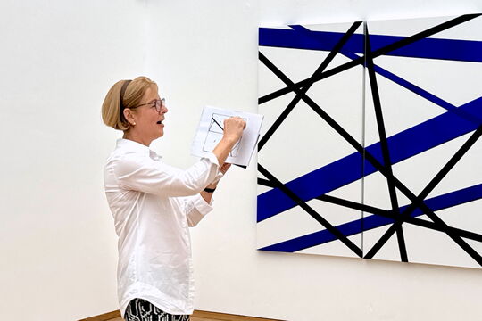 Die Kuratorin erklärt bei der Vernissage das Arbeitsprinzip "System und Zufall" von Norbert Thomas